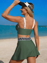 Woman in green two-piece swimsuit on a beach with clear blue water and sky.