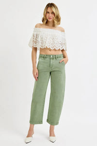 Woman wearing a white lace off-shoulder top and green pants on a white background