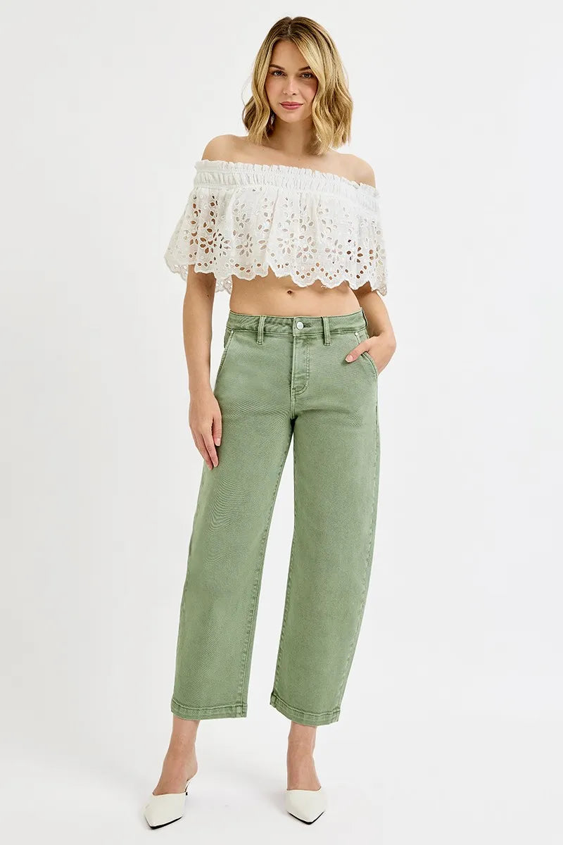Woman wearing a white lace off-shoulder top and green pants on a white background