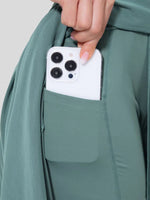 Person placing a smartphone into a pocket of a green jacket