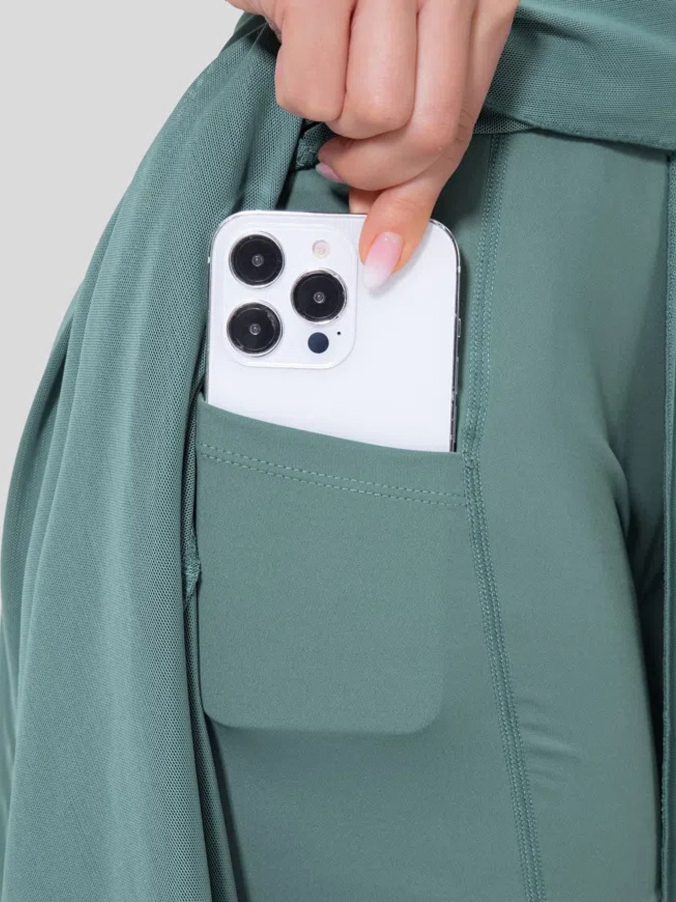 Person placing a smartphone into a pocket of a green jacket