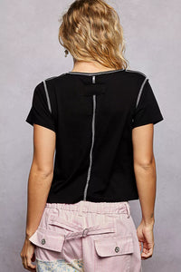 Person wearing a black top with white accents and pink pants on a gray background