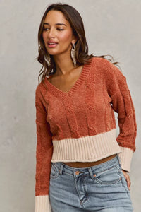 Woman wearing a two-tone sweater with rust and beige colors, paired with blue jeans against a neutral background.