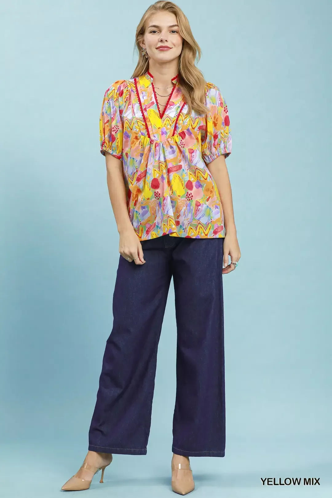 Woman wearing a colorful blouse and navy pants against a light blue background