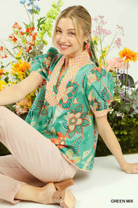 Woman wearing a colorful floral blouse sitting among flowers with 'Green Mix' text.