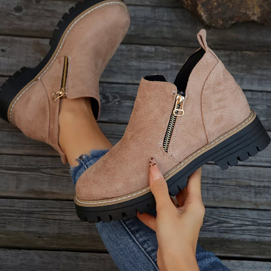 Beige ankle boots with gold zippers on a wooden floor