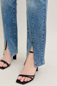 Close-up of blue jeans with a slit and black high-heeled sandals on a light gray background