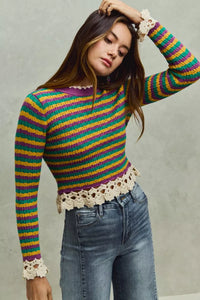 Woman wearing a colorful striped sweater with lace details against a neutral background