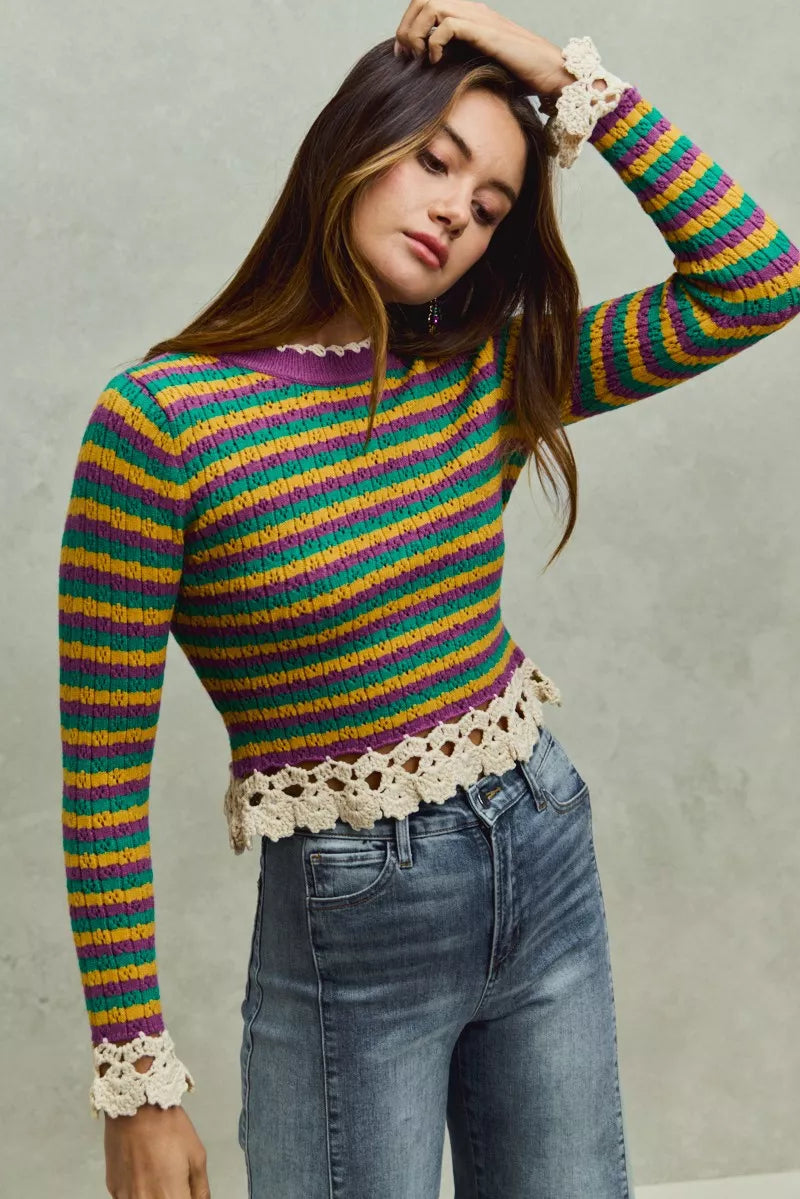 Woman wearing a colorful striped sweater with lace details against a neutral background