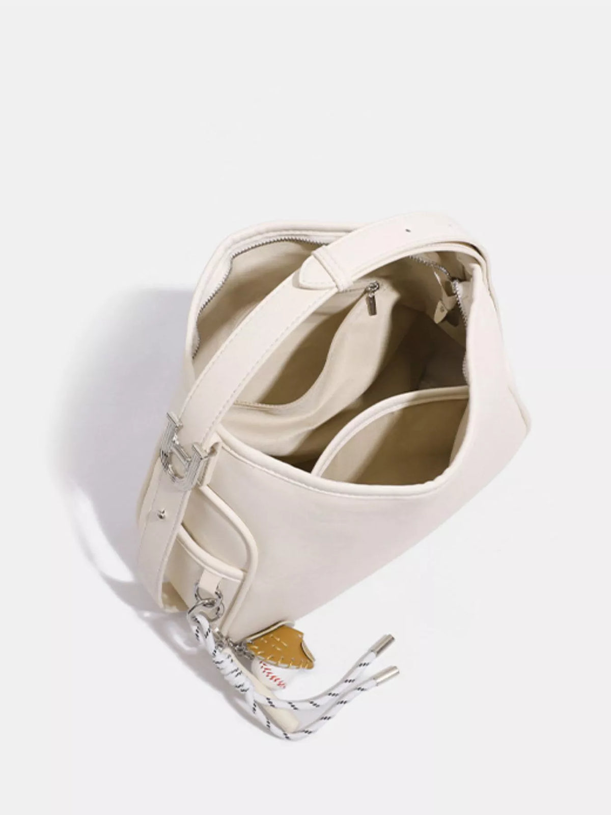 An off-white leather shoulder bag with silver hardware and a patterned tassel, shown from an overhead angle on a light gray background.