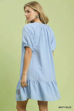 Woman wearing a light blue dress with ruffled sleeves and hem on a green background