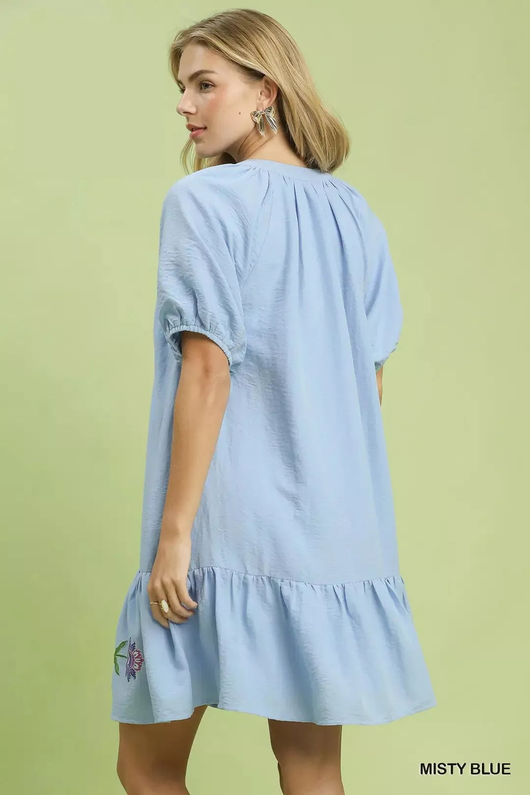Woman wearing a light blue dress with ruffled sleeves and hem on a green background