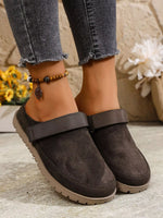 Brown suede shoes worn with ripped jeans on a light surface.