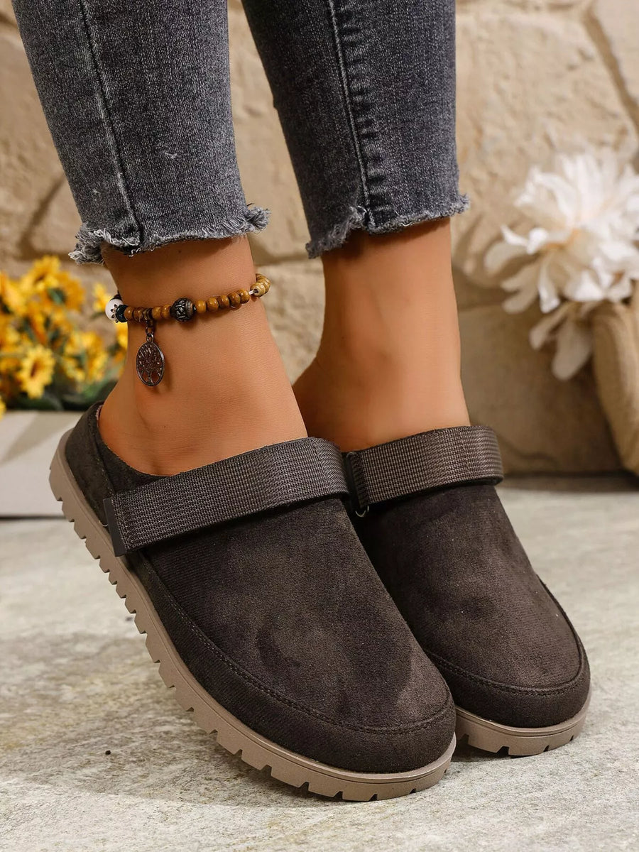 Brown suede shoes worn with ripped jeans on a light surface.