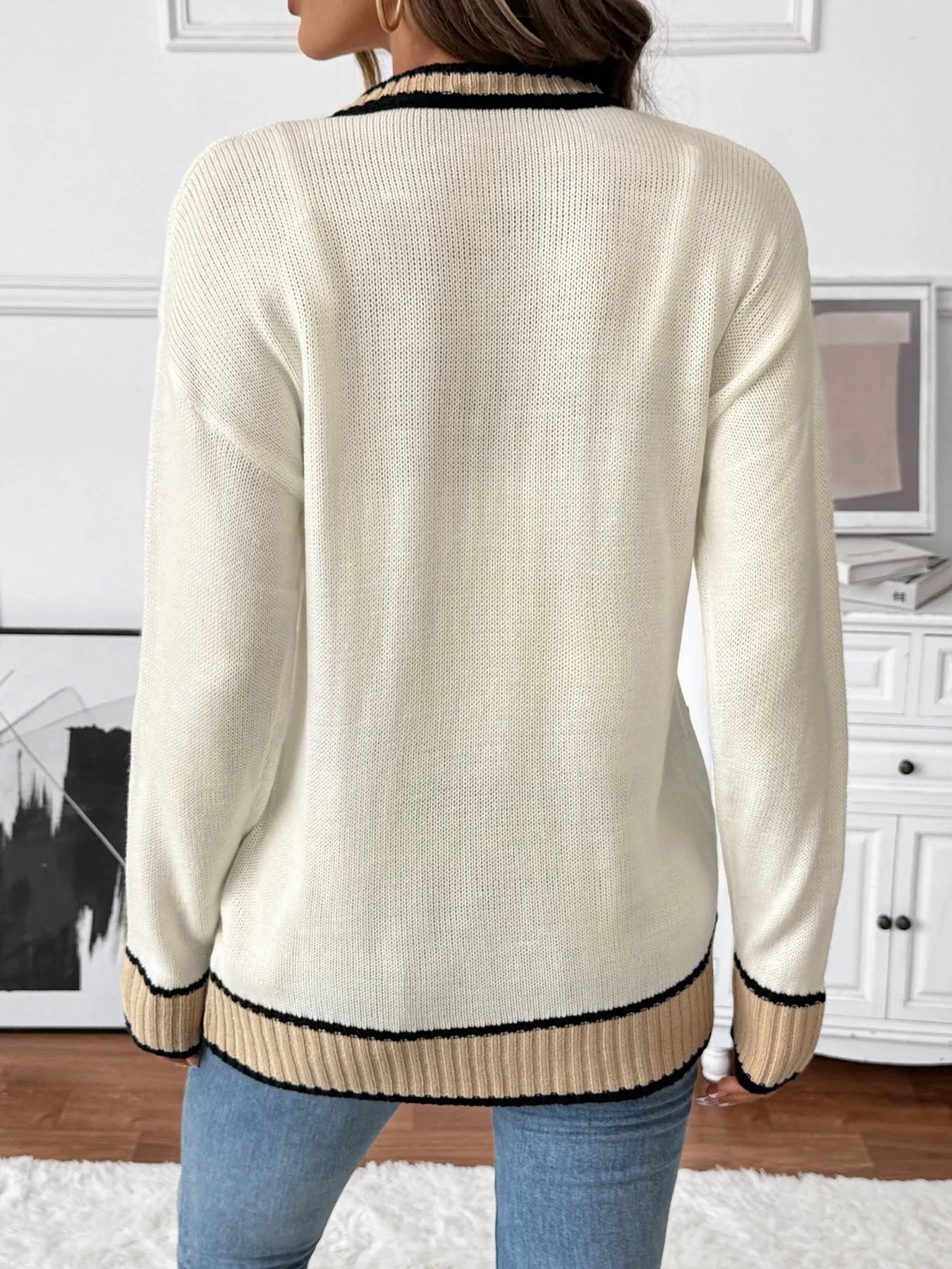 Person wearing a cream-colored sweater with black trim in a room setting.