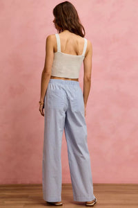 Woman wearing a beige tank top and light blue checkered pants against a pink wall.