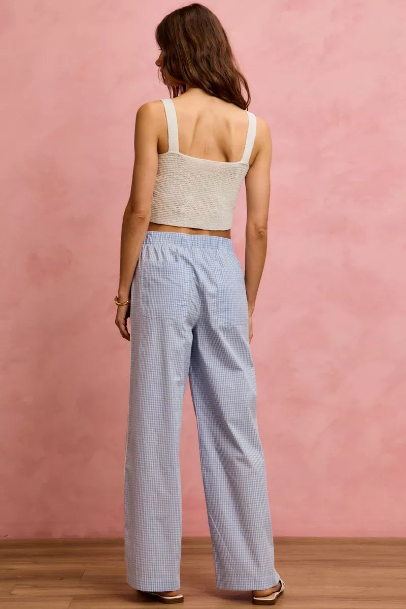 Woman wearing a beige tank top and light blue checkered pants against a pink wall.