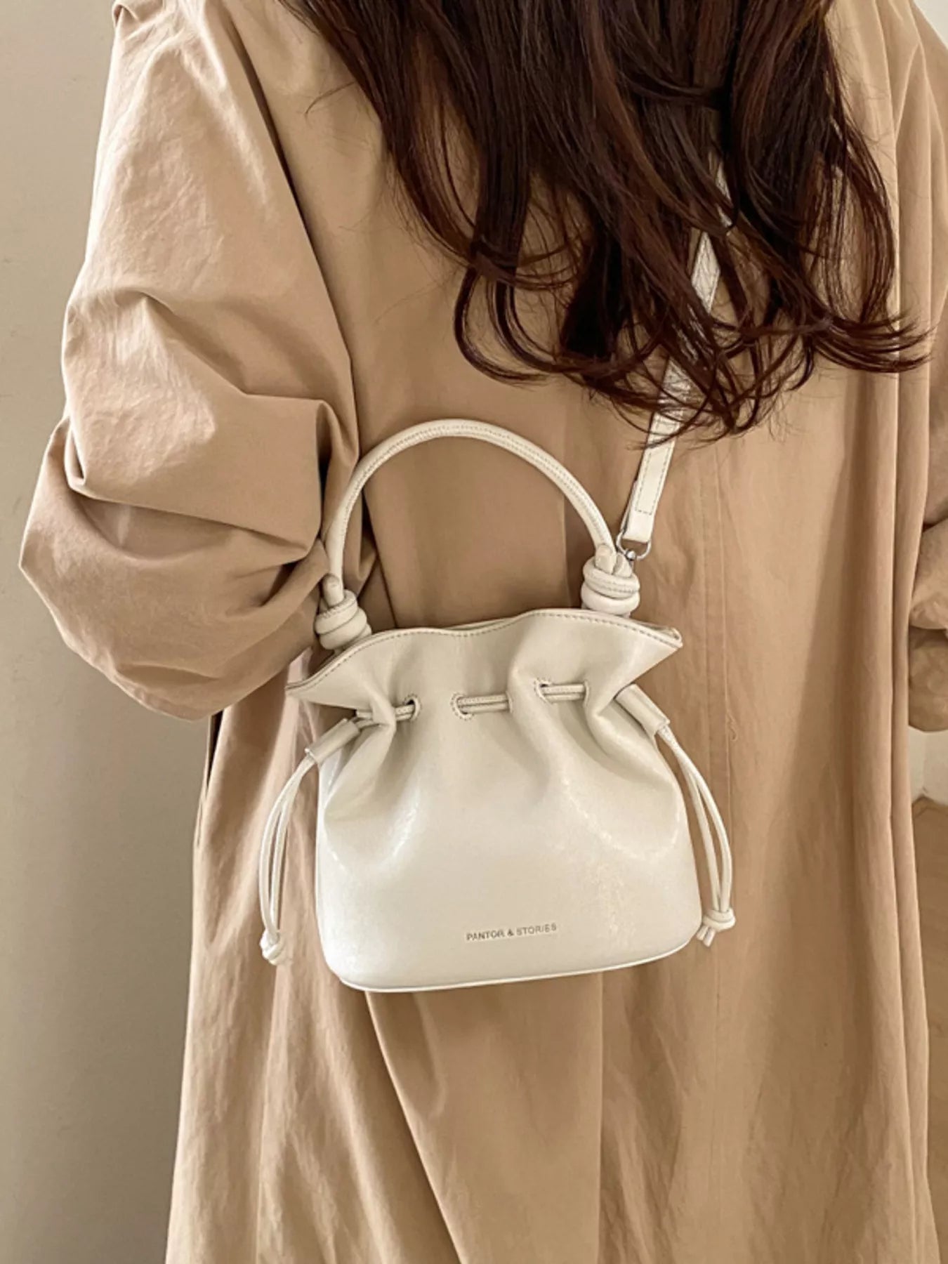 White drawstring bag held by a person wearing a beige coat against a neutral background
