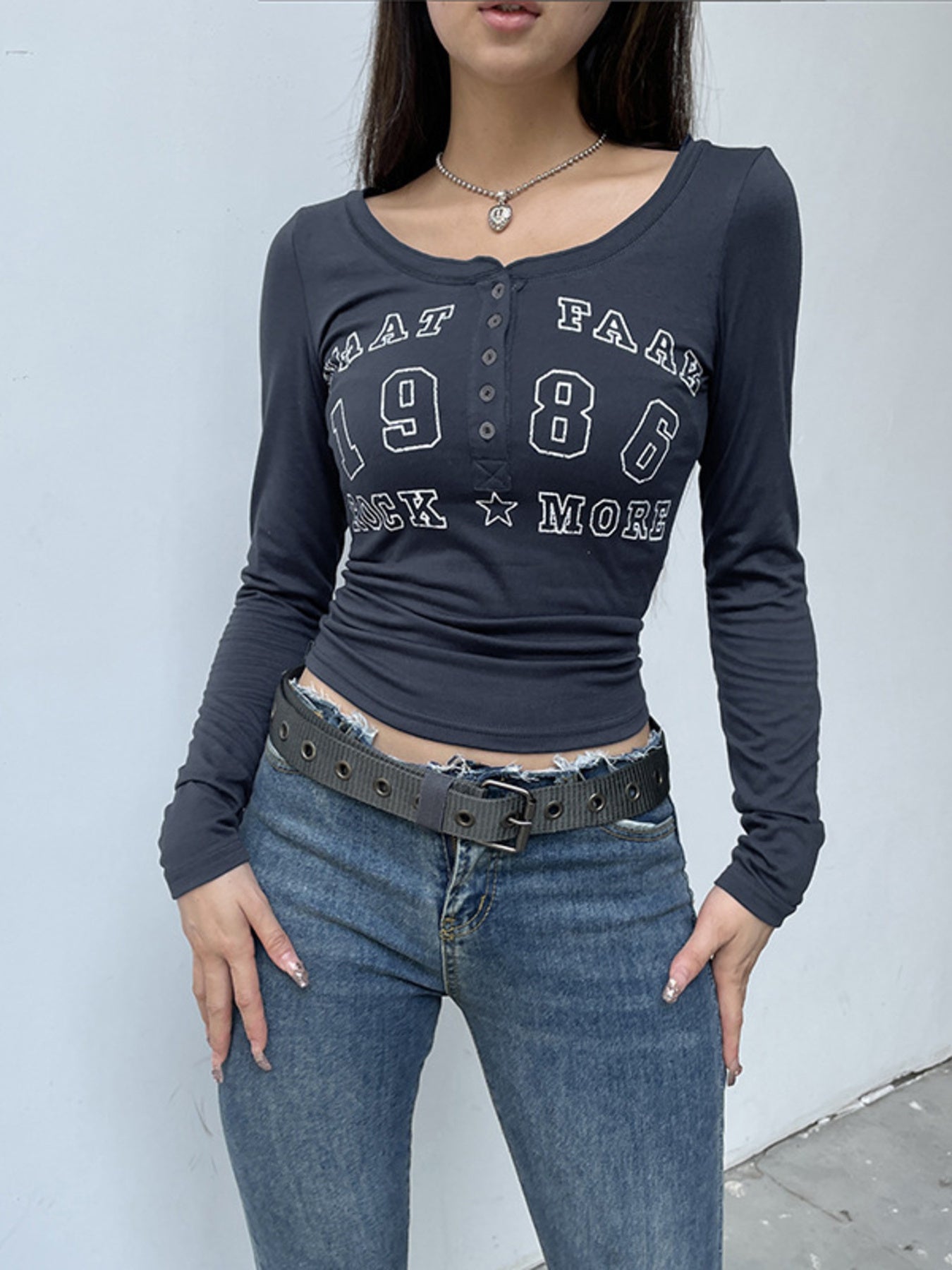 Person wearing a dark long-sleeve shirt with text and jeans against a light gray background