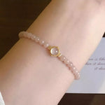 Bracelet with pink beads and a gold clasp on a wrist, with a blurred background.