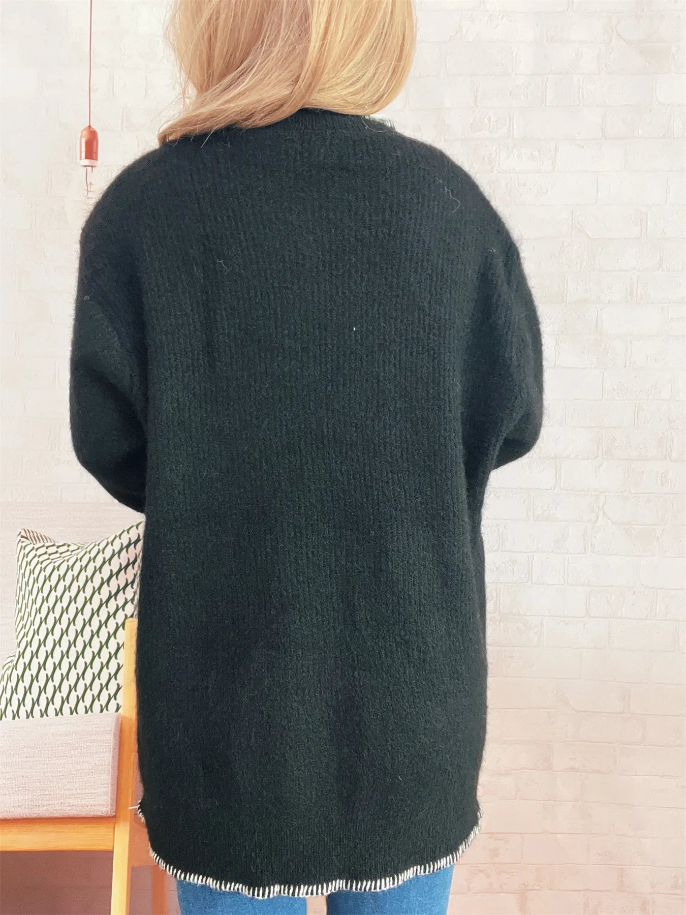 Person wearing a dark green cardigan in a room with a chair and decorative items.
