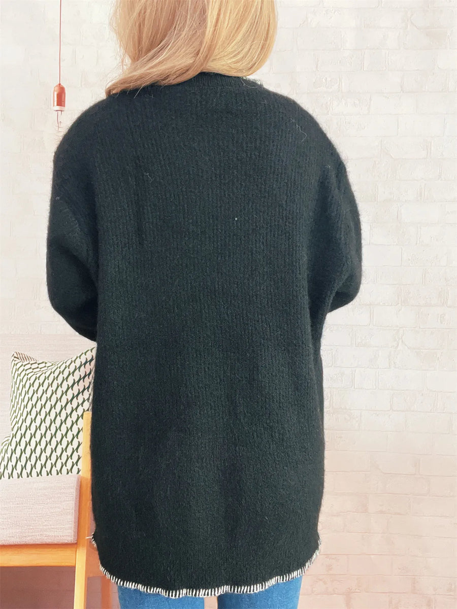 Person wearing a dark green cardigan in a room with a chair and decorative items.