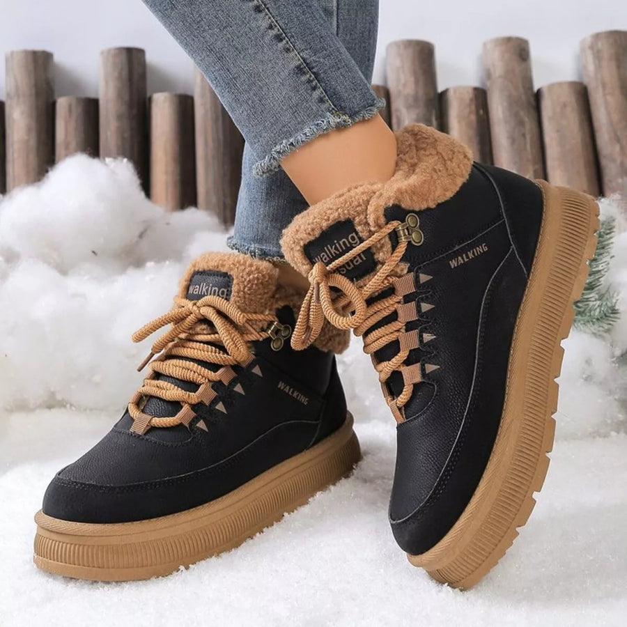 Black winter boots with brown fur lining and soles worn by a person on a snowy background.