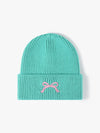 Turquoise knit beanie with a pink bow on a light gray background