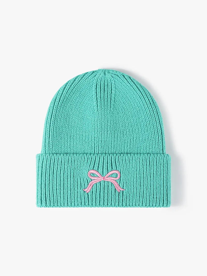 Turquoise knit beanie with a pink bow on a light gray background