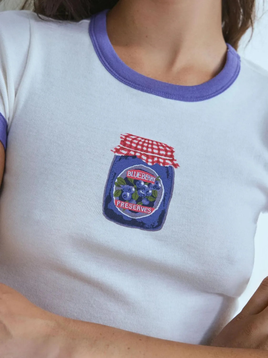 White t-shirt with a blueberry preserves patch on a person wearing a purple shirt.