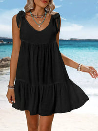 Woman wearing a black dress on a beach with clear blue water and sky.