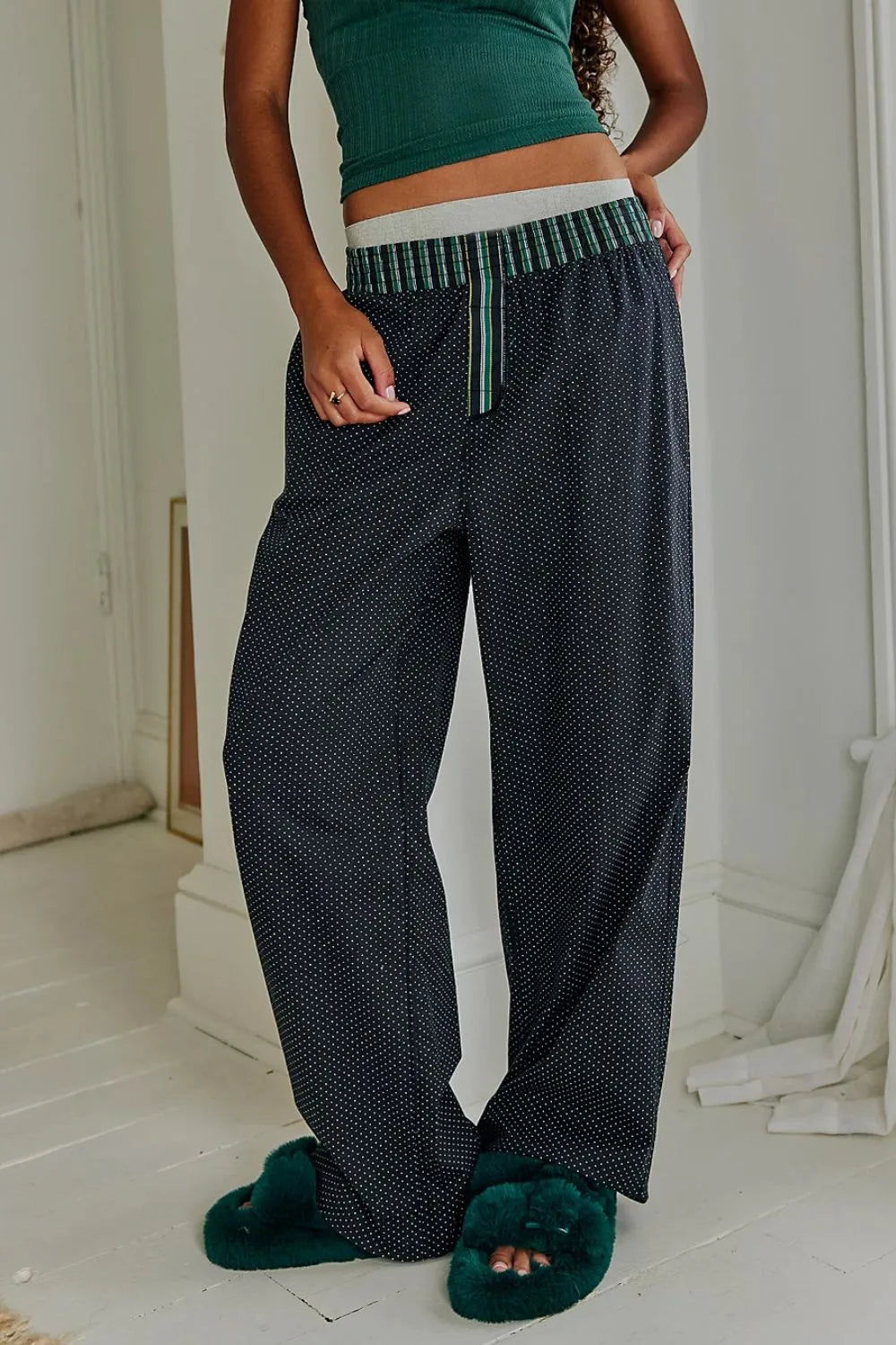 Person wearing dark patterned pants and green top in a minimal indoor setting