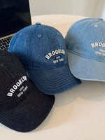 Three denim baseball caps with 'Brooklyn New York' text on a light surface.