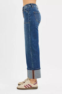 Blue jeans with a cuffed hem worn by a person on a white background