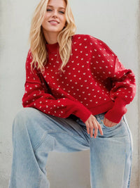 Woman wearing a red sweater with white patterns and light blue jeans against a plain background