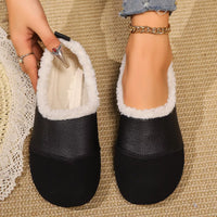 Black slippers with white fur lining worn by a person on a textured surface.
