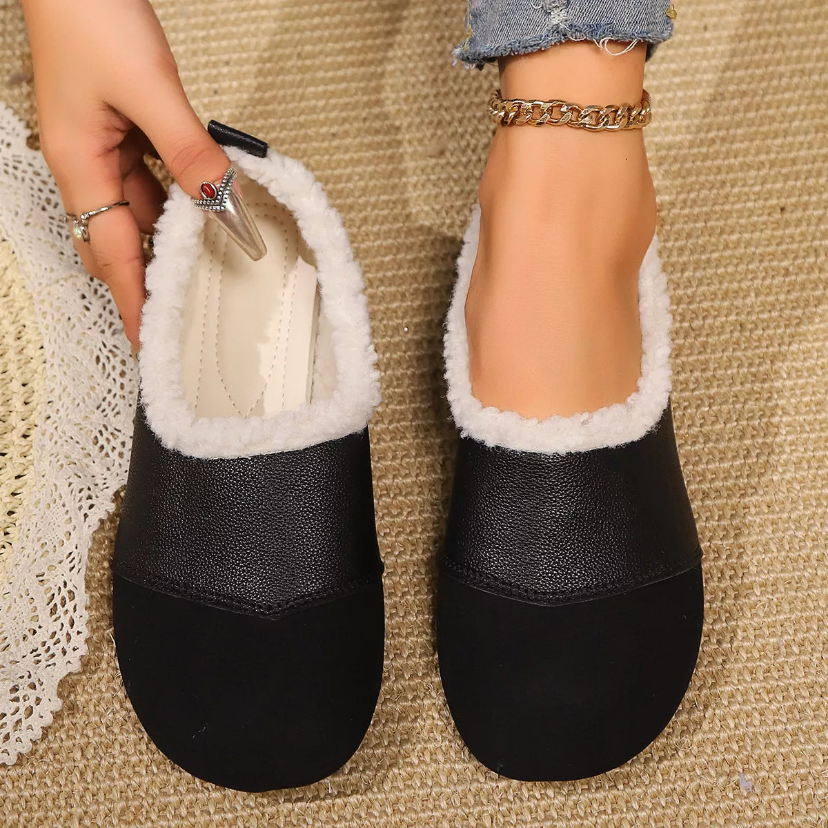 Black slippers with white fur lining worn by a person on a textured surface.