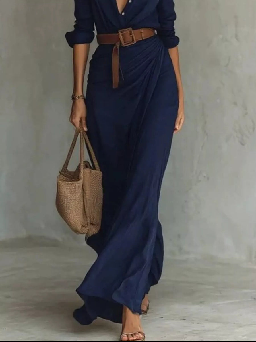 Woman wearing a navy blue dress with a brown belt and holding a woven bag against a neutral background