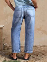 Person wearing light blue jeans standing against a beige wall.