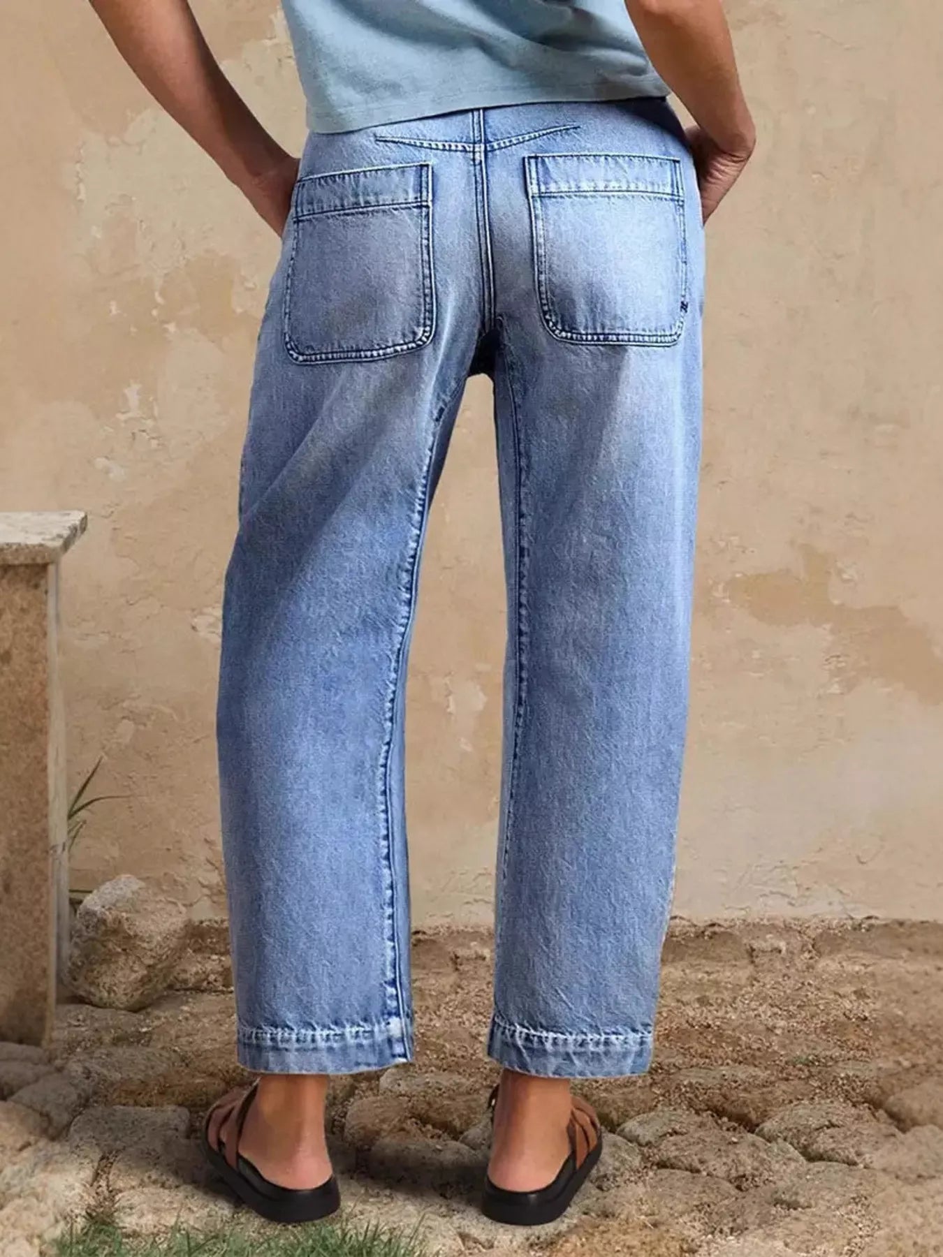 Person wearing light blue jeans standing against a beige wall.