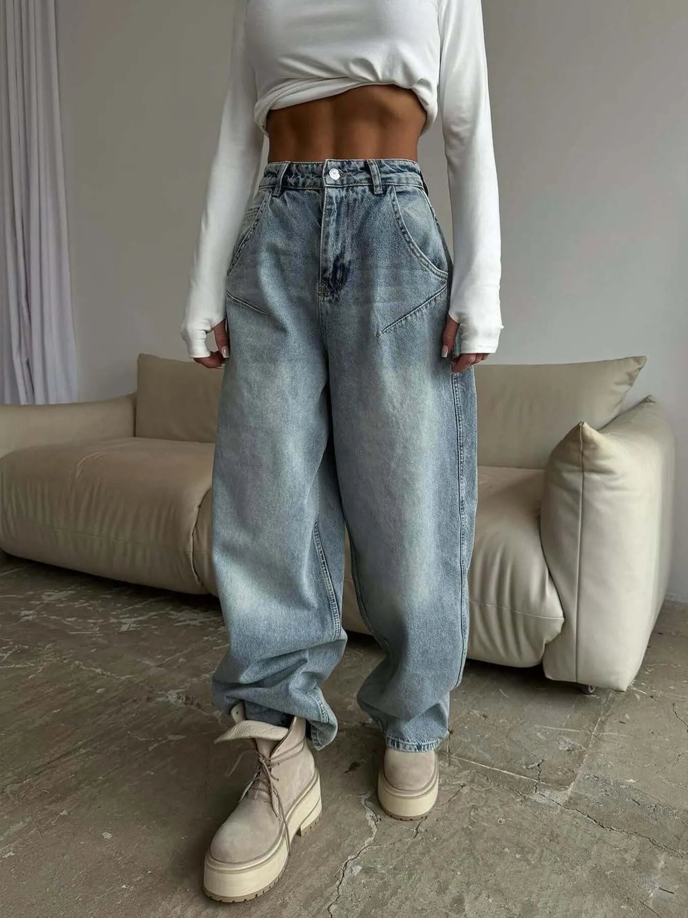 Person wearing a white long-sleeve top and blue jeans in a room with a beige sofa.