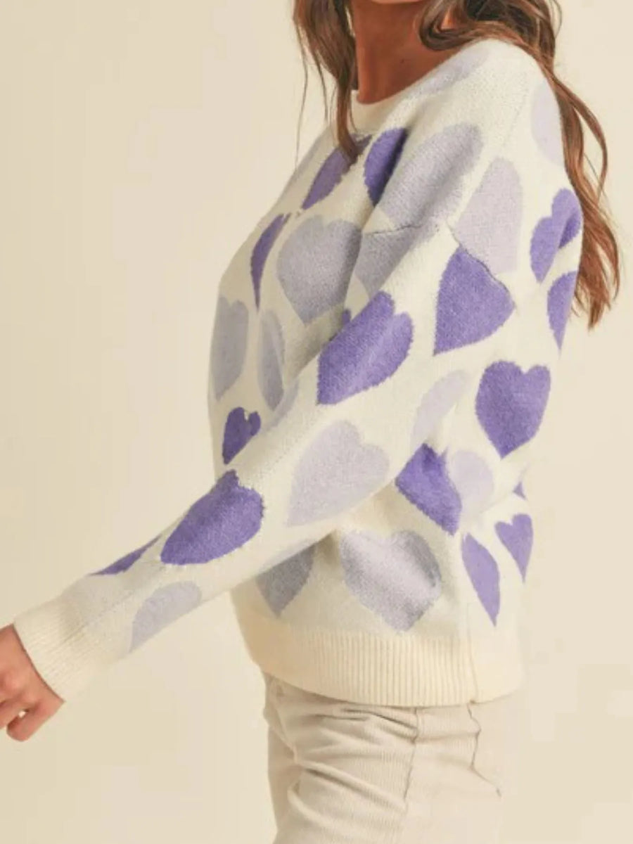 Person wearing a white sweater with purple heart patterns on a plain background