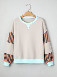 Beige sweatshirt with striped sleeves on a hanger against a light gray background