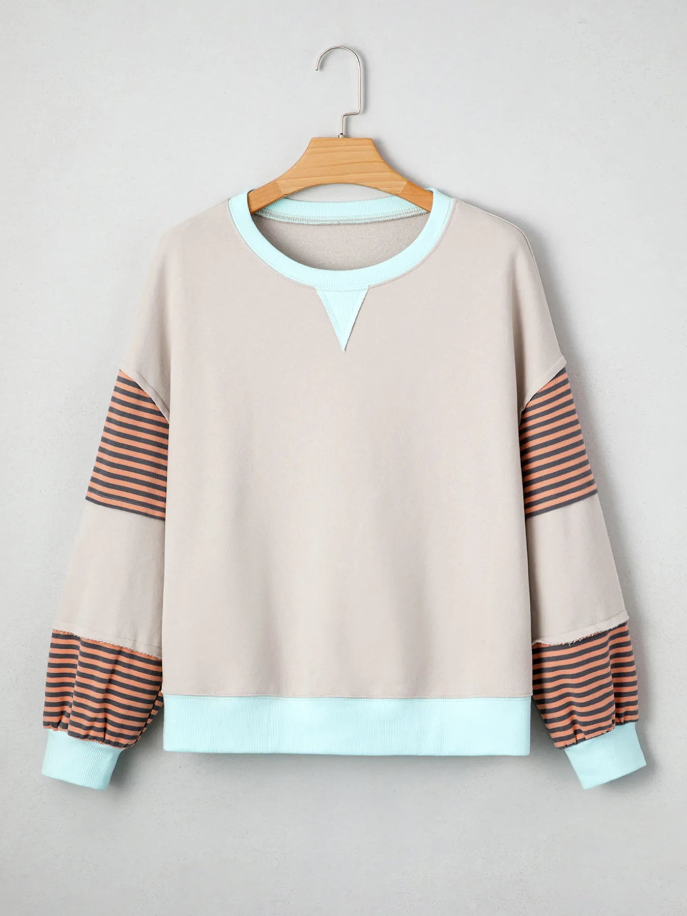 Beige sweatshirt with striped sleeves on a hanger against a light gray background