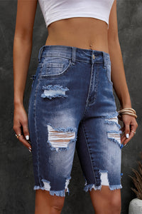 Person wearing distressed blue denim shorts on a dark background