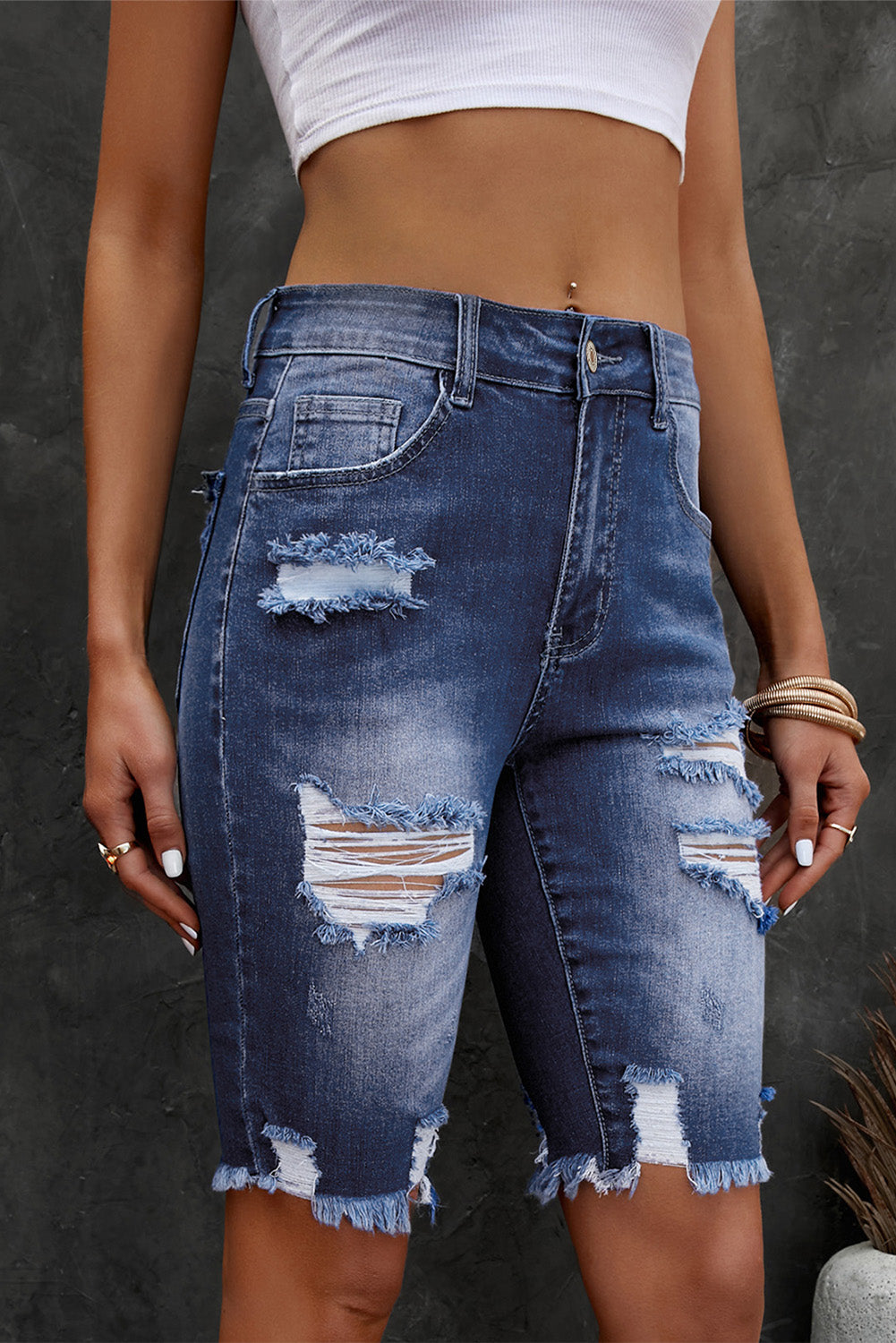Person wearing distressed blue denim shorts on a dark background