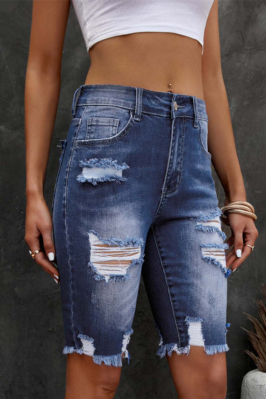 Person wearing distressed blue denim shorts on a dark background