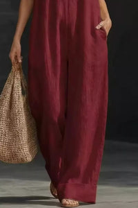 Person wearing a burgundy jumpsuit holding a woven bag against a dark background