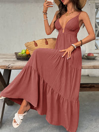 Woman in a long rust-colored dress sitting outdoors with a wooden table and fruit basket in the background.