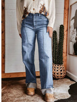 Person wearing blue jeans and a patterned shirt in a room with a cactus plant and framed picture.